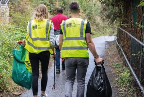 Two people walking in high-vis jackets with litterpicking gear